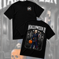 Two black short-sleeve graphic T-shirts shown against a blurred Halloween-themed background. The front shirt has a small circular 'SMC' logo on the chest, and the back shirt features a large 'HALLOWEEN II' graphic with an illustrated character in a dark outfit holding a pumpkin.